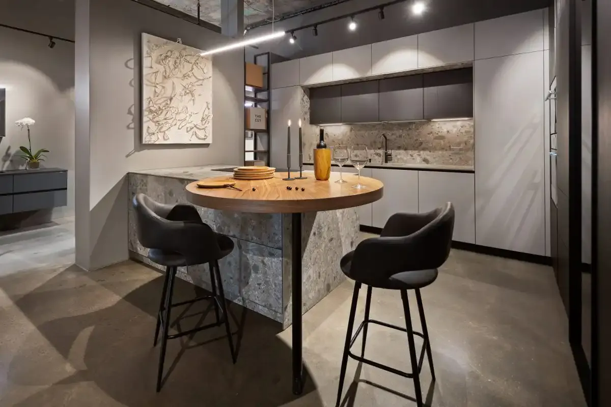 The kitchen display at the European Kitchen Center showroom: a stone-clad island with a round wood top and two stools